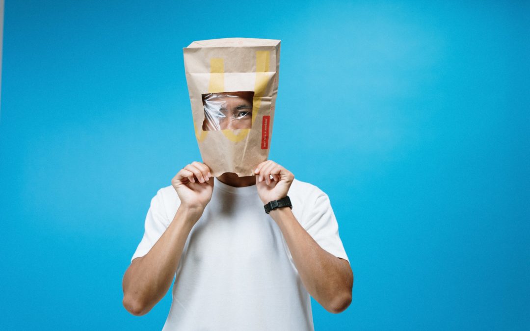 A person wearing a paper bag on their head in front of a blue background