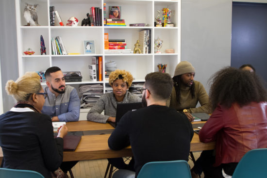 A diverse group ofyoung people of color sitting around a table deep in discussion.